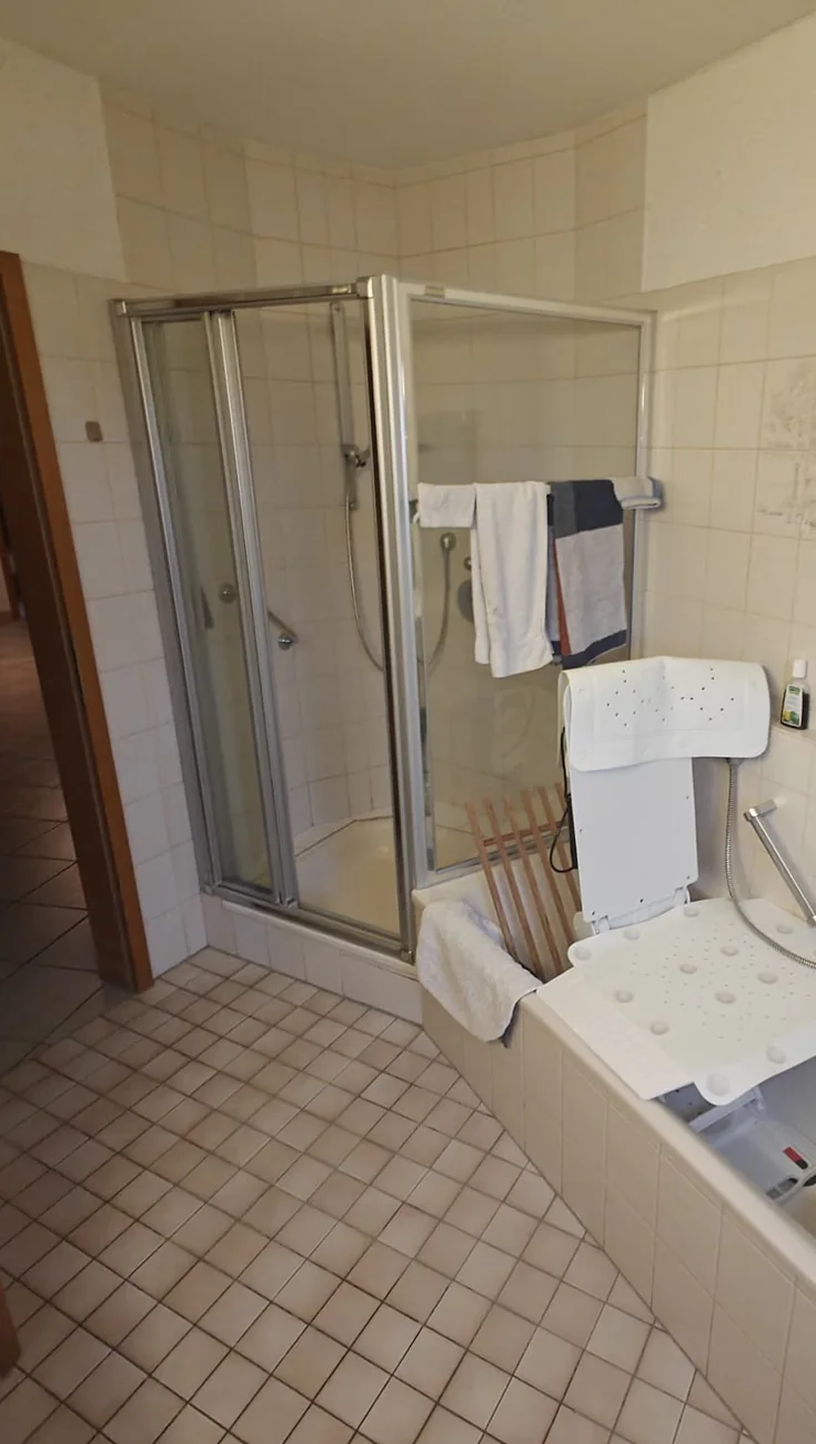 Altes Badezimmer vor dem barrierefreien Umbau mit enger Duschkabine und Badewannenlift